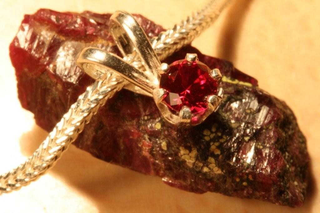A gold ruby pendant, pictured over uncut raw ruby.